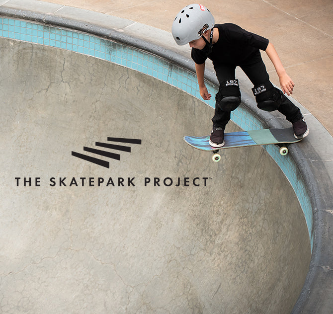 A young skateboarder in a helmet and pads rides a skateboard in a concrete skatepark bowl, with "THE SKATEPARK PROJECT" logo visible.