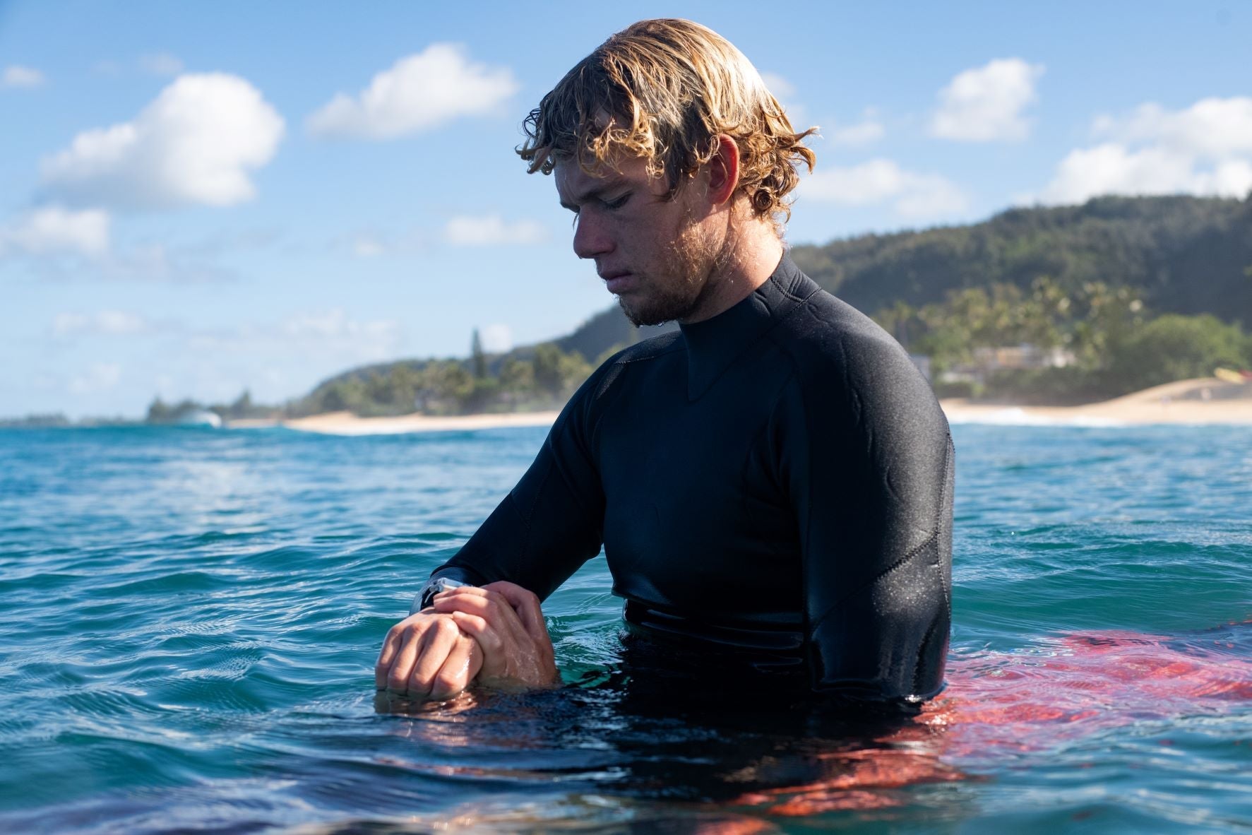 Surfer John John Florence sits in the water and uses his Nixon Surf watch