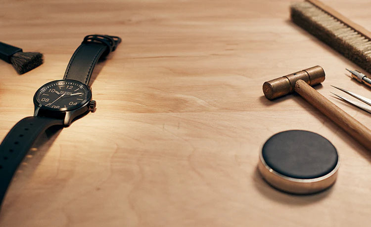 Tools and a Nixon watch sit on a wooden table.